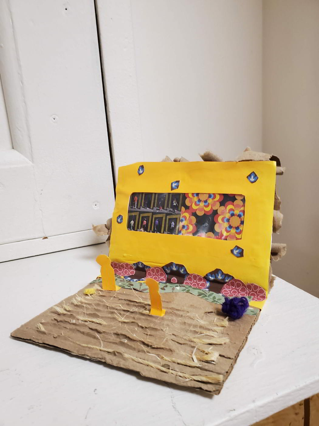 A cardboard Book shaped mini theater / laptop with a yellow background and cut out figures.